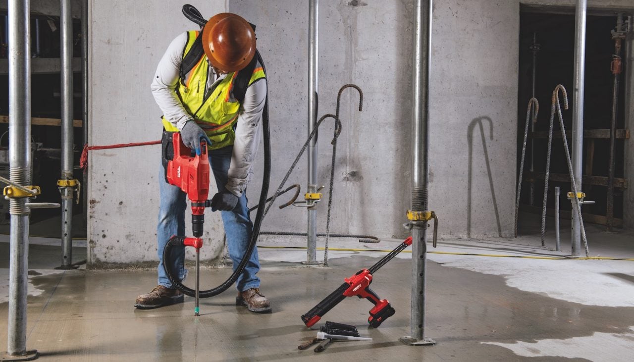 Construction worker using Hilti SafeSet installation method with VC 140-2-22 "vac-pack" vacuum and TE 60-22 cordless rotary hammer. HDE 500-22 cordless adhesive dispenser, HIT-RE 100 adhesive anchor